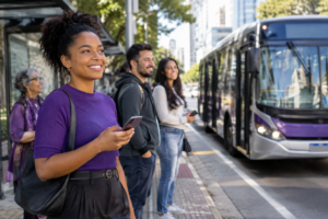 Cena fotográfica real em São Paulo: pessoas brasileiras adultas aguardam em um ponto, em clima positivo, enquanto um ônibus de verdade se aproxima; sem telas visíveis, ilustrações ou montagens.