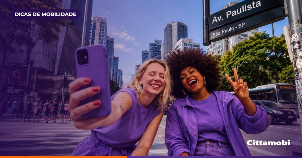 Passageiros em um ponto de ônibus de São Paulo consultam o celular enquanto um ônibus se aproxima.